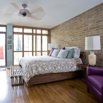 a bedroom with a bed, purple chair and brick wall