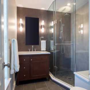 Newly remodeled bathroom with dark brown vanity and a glass door shower.