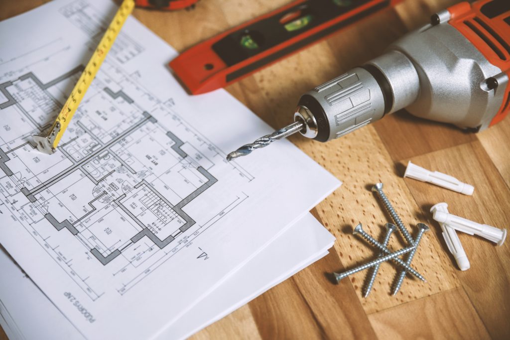 Blue print of home remodel design on table next to drill and leveler.